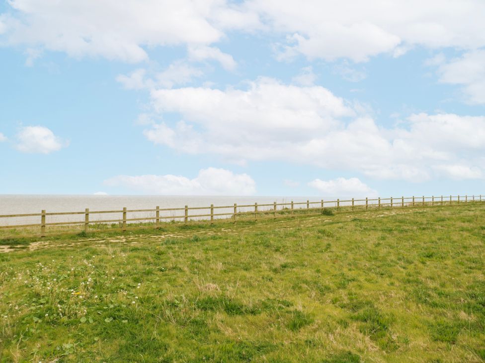 A grassy area with a wooden fence and sea in the background at 59 Cliff Field in Lowestoft