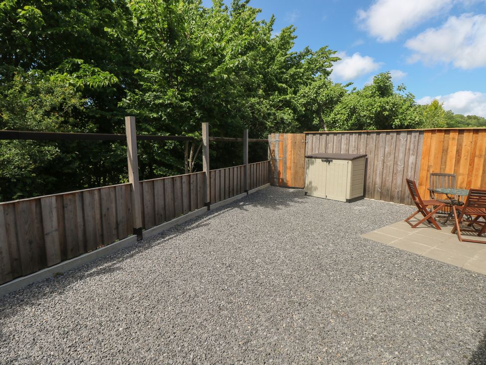 An outdoor garden area with a gravel surface and wooden furniture at Brookview Goldfinch in Haverfordwest