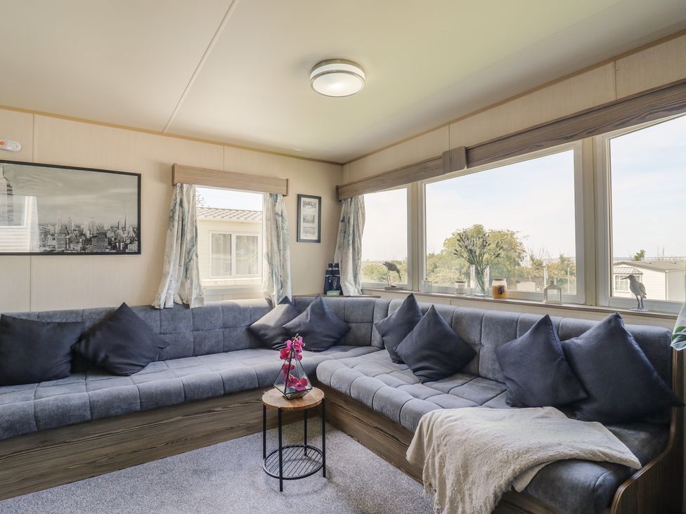 A living room with a sectional sofa and windows at Estuary View in Allhallows