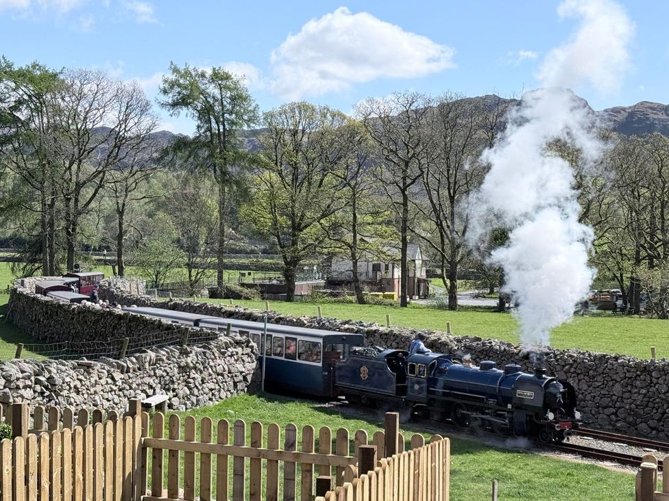 A steam train on a track with a stone wall and trees at Pandora in Holmrook