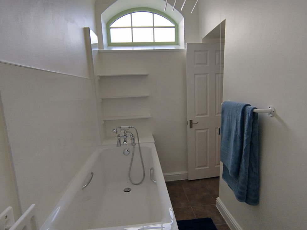 A bathroom with a bathtub and shelves at Linhay Barn Saltash
