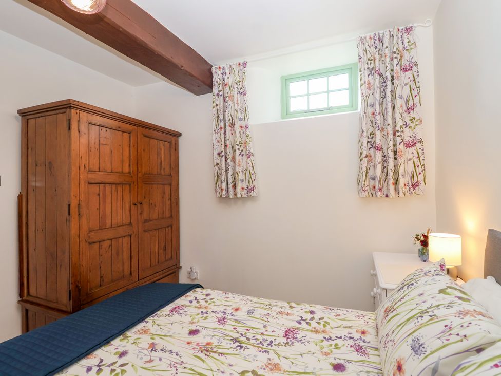 A bedroom with a bed and wooden wardrobe at Linhay Barn in Callington