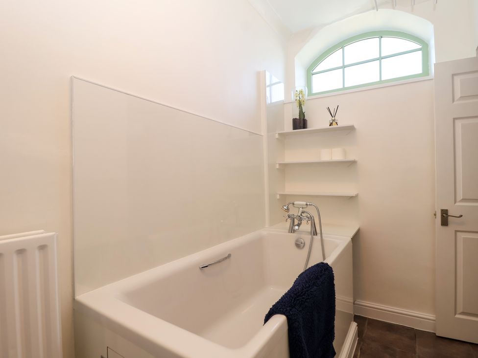 A bathroom with a bath tub and shelves at Linhay Barn in Callington
