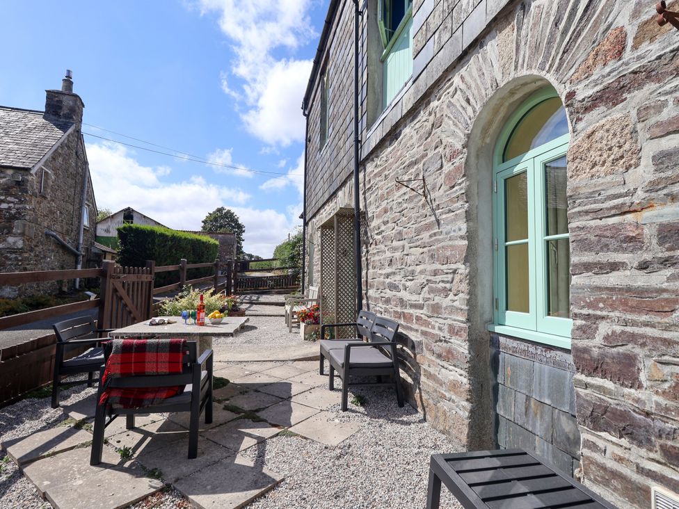An outdoor seating area with a stone wall and table at Linhay Barn in Callington