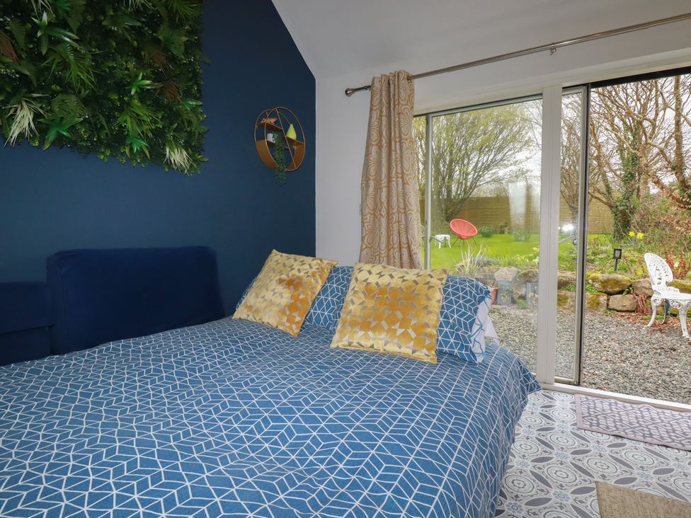 A bedroom with a bed and window leading to a garden at Little Hallegan in Camborne