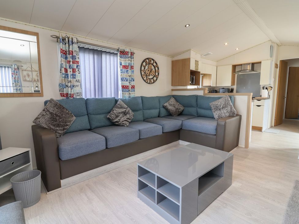 A living room with a sectional sofa and a kitchen area at Carvan CP10 Prestatyn