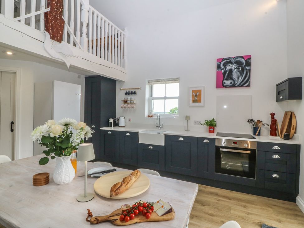A kitchen with a table, chairs, and a refrigerator at The Byre in Conwy