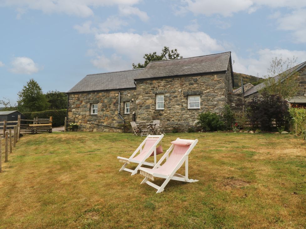 An outdoor area with a stone building and deck chairs at The Byre in Conwy