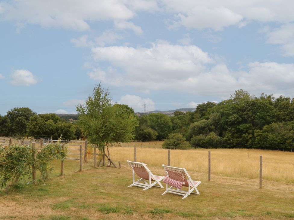 A view of two deck chairs on grass with trees and a field at The Byre in Conwy