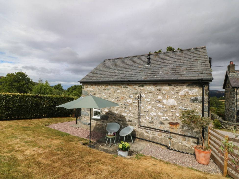 A garden with a stone building and seating area at Little Oak near Tal-Y-Bont