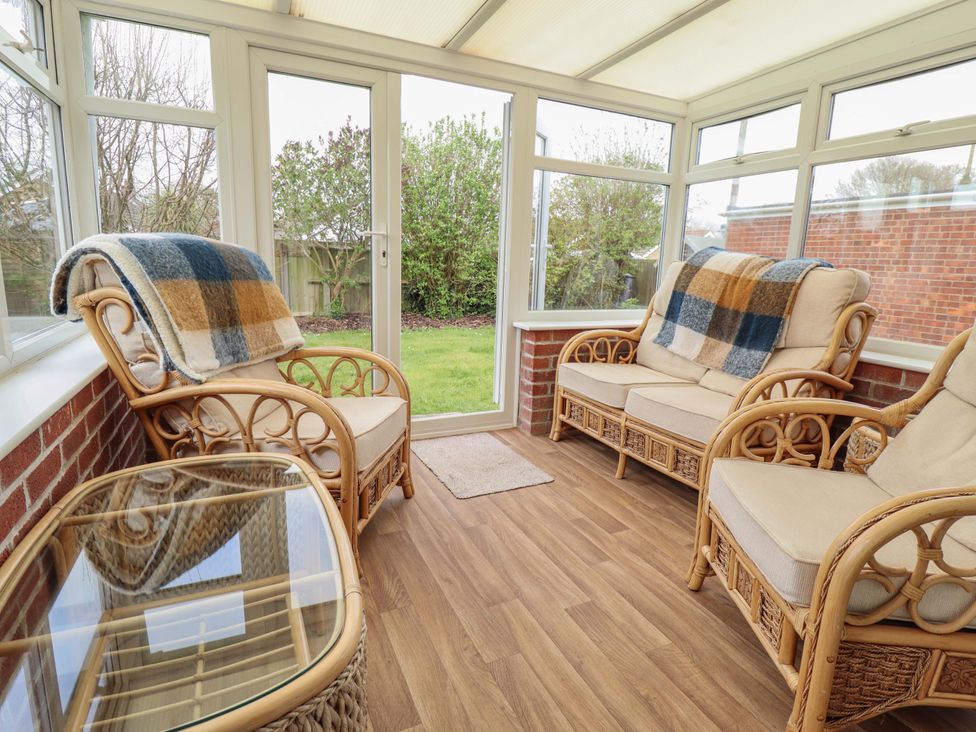 A conservatory with rattan chairs and a glass table at Field View in North Walsham