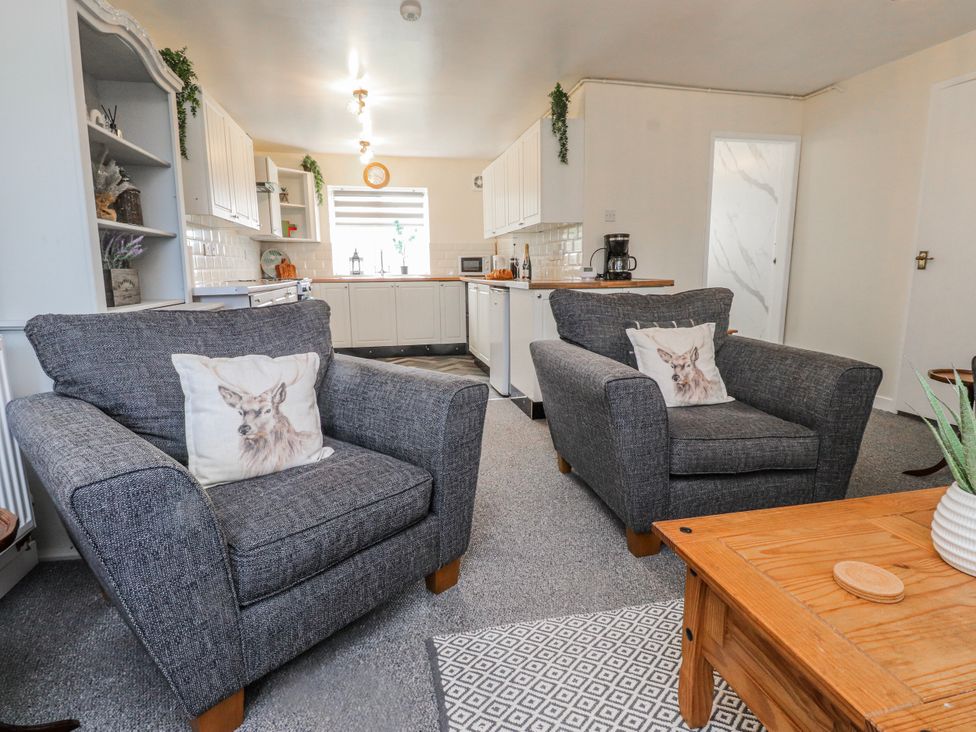 A living room with gray sofas and a kitchen in the background at Hen Fecws Rhoshirwaun near Sarn Meyllteyrn