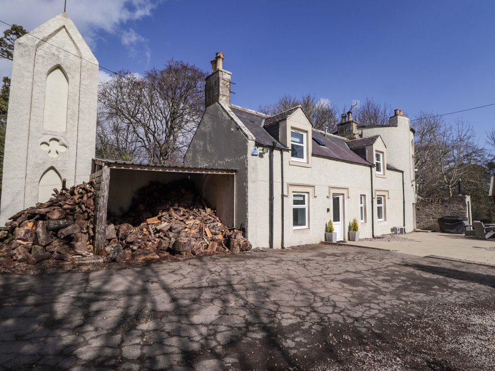 A house with a woodpile and parking area at Craig Cottage in Banff