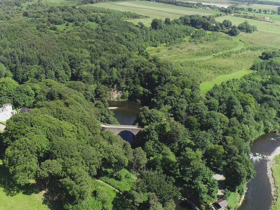 An aerial view of a river with a bridge and surrounding forest at Craig Cottage in Banff