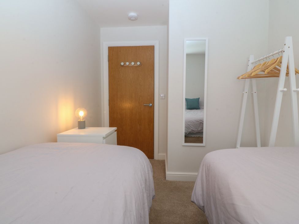 A bedroom with two beds, a lamp, nightstand, and door at 2 Ocean View, Colwyn Bay