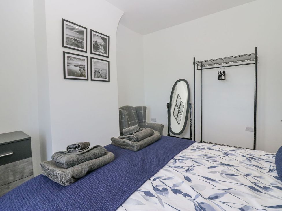 A bedroom with a bed, chairs, towels, and photographs at Victroneen Cottage in Whitehaven