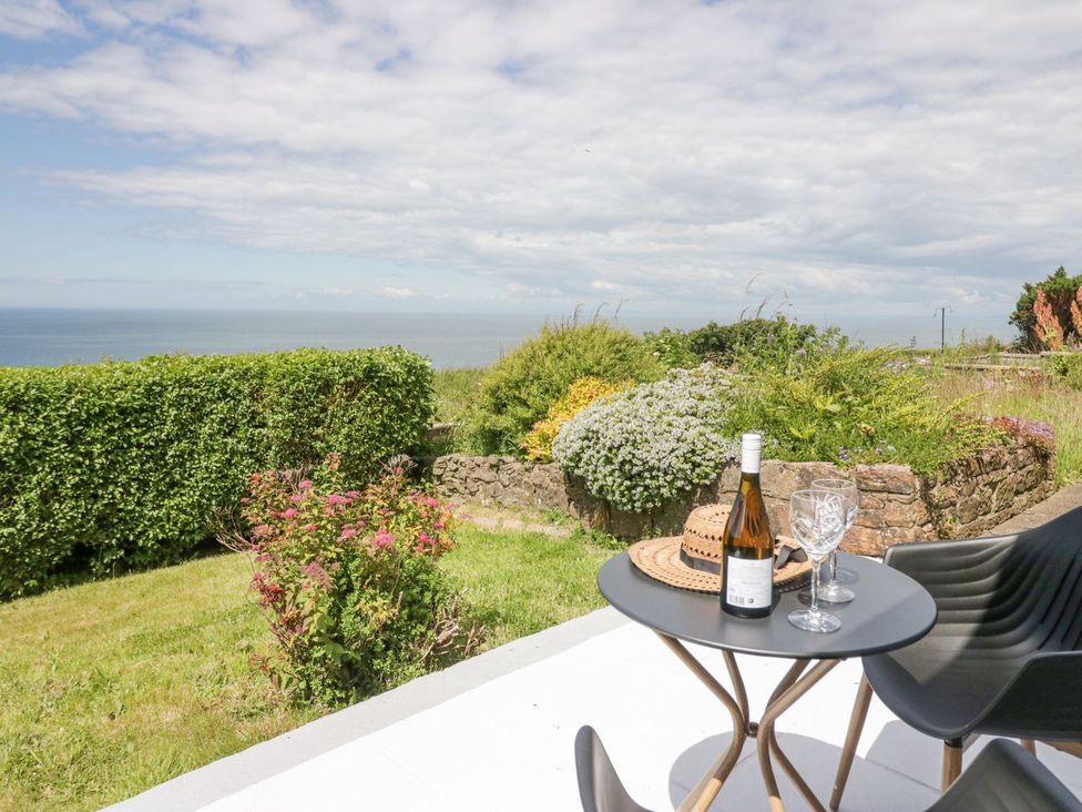 A garden with a table, wine, glasses, and ocean view at Victroneen Cottage Whitehaven