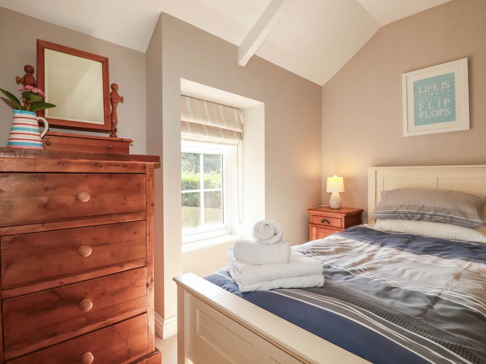 A bedroom with a bed, dresser, towel, and lamp at Bryher Cottage in St Mawgan