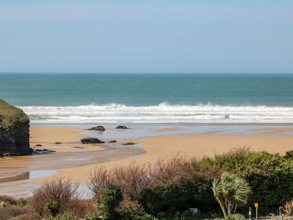 A beach with waves and rocks at Bryher Cottage in St Mawgan