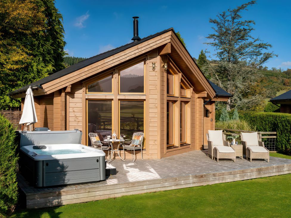 An outdoor area with a hot tub and dining furniture at Cwtch Log Cabin in Llandrillo
