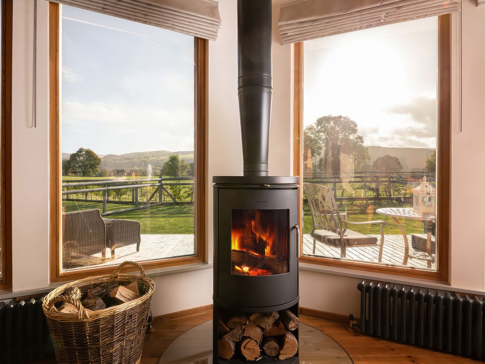 A living room with a wood stove and a firewood basket at Cwtch Log Cabin Llandrillo