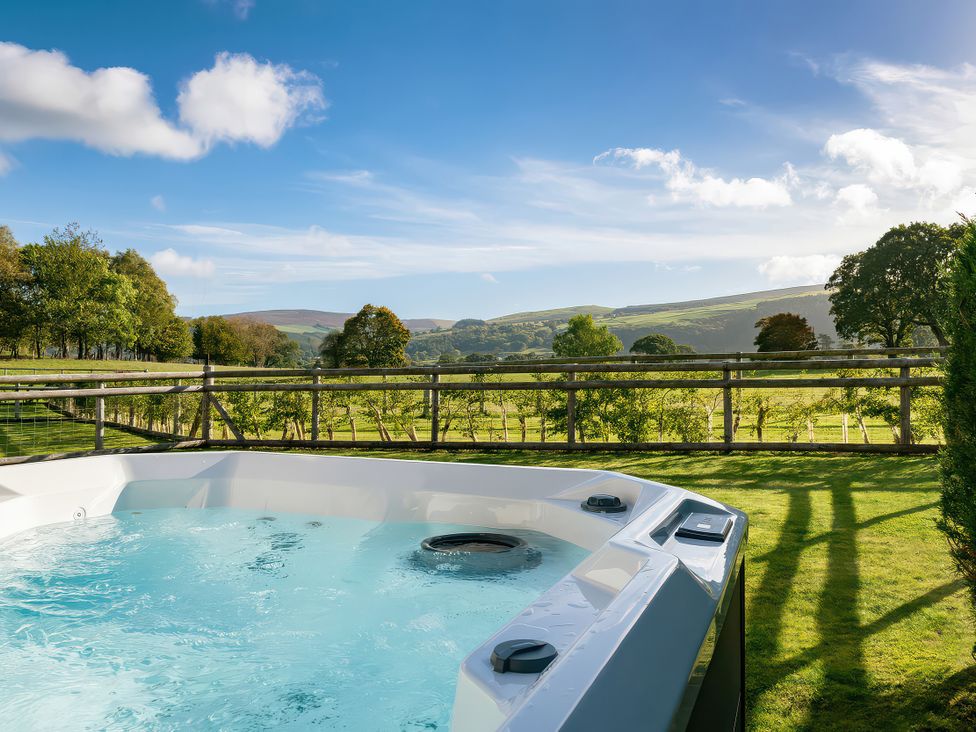 A hot tub with a view of hills and trees at Cwtch Log Cabin Llandrillo