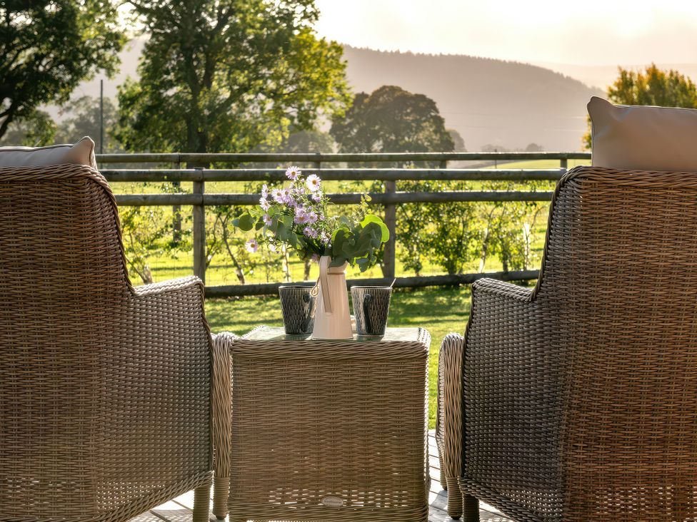 Outdoor seating area with two armchairs and a table holding a vase with flowers at Cwtch Log Cabin Llandrillo