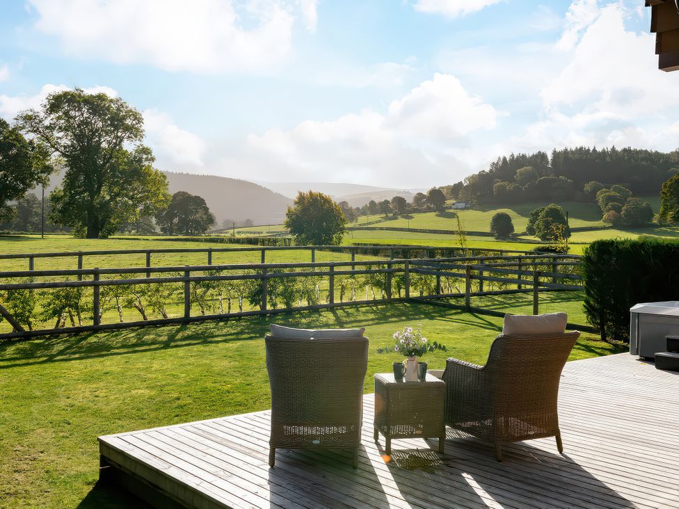 A deck with chairs and a table overlooking fields at Cwtch Log Cabin in Llandrillo