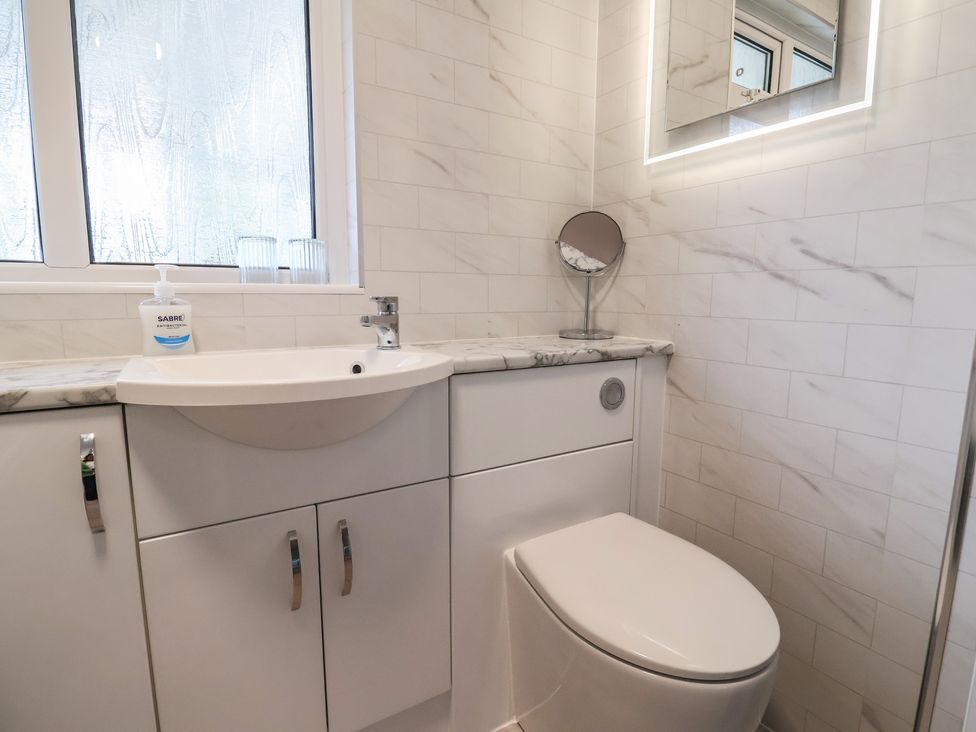 A bathroom with a sink, toilet, mirror, and window at 2 North Road, Maiden Newton, Dorset
