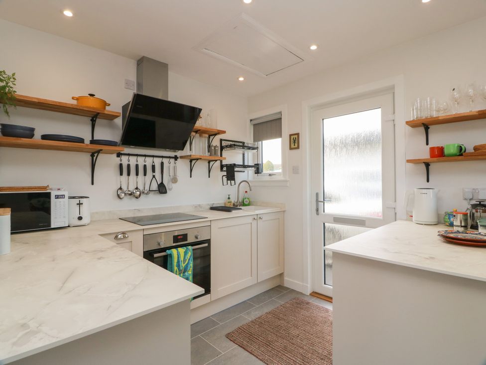 A kitchen with modern appliances and wooden shelves at 15 Laigh Isle