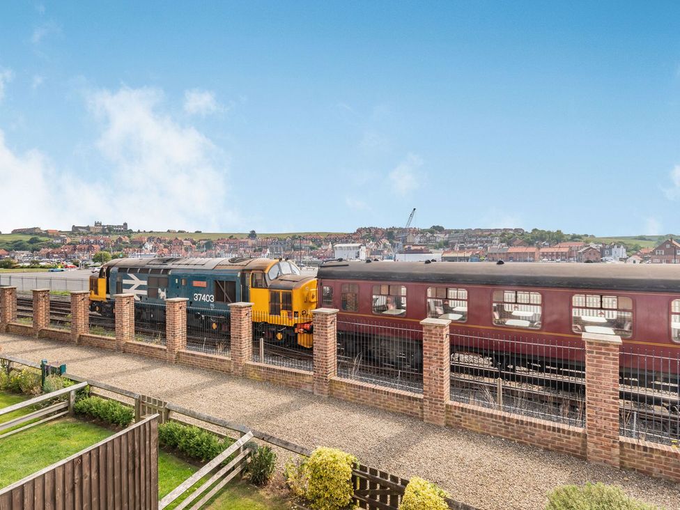 A train passing by near a fence and grass area at Rails End