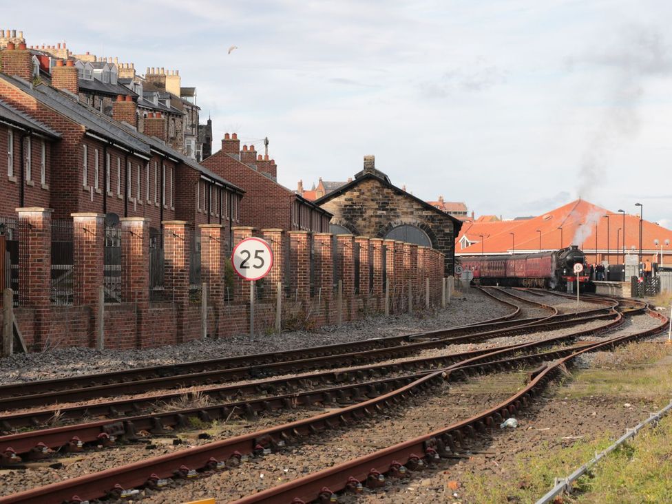A train passing by houses and a speed limit sign near a railway station at Rails End 