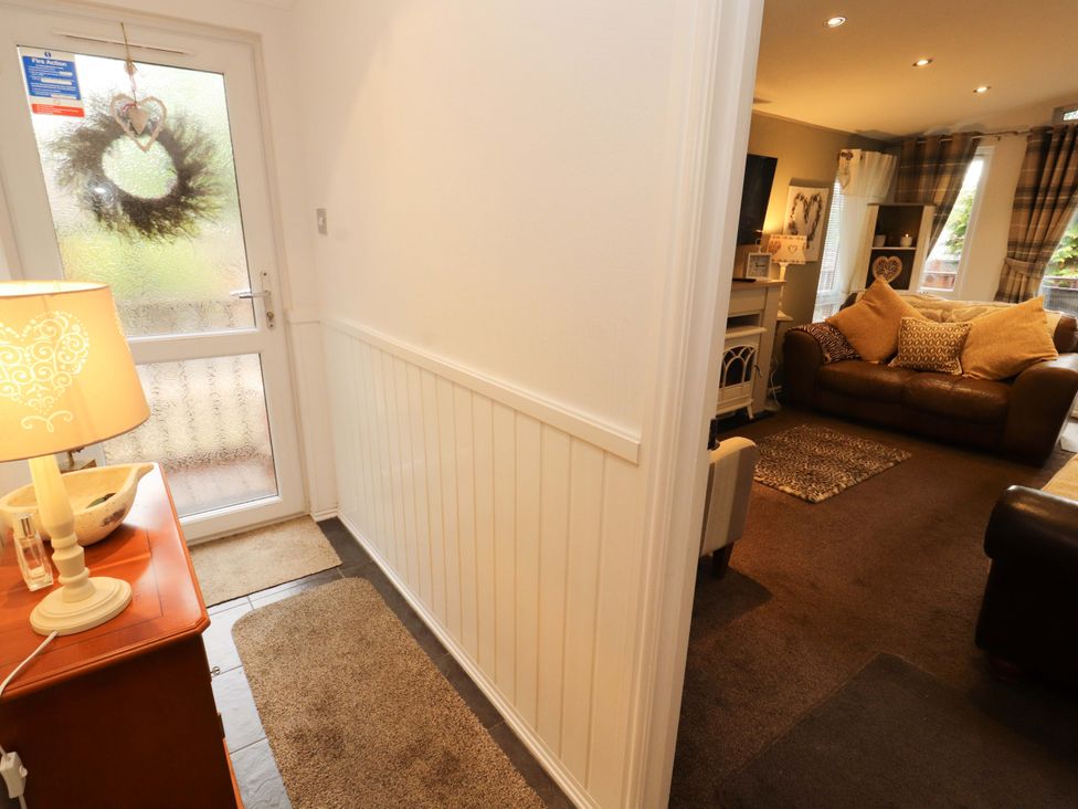 A hallway with a door, rug, lamp, and view of a living room at Jodene Lodge, Redwood 2 in Bowness-On-Windermere
