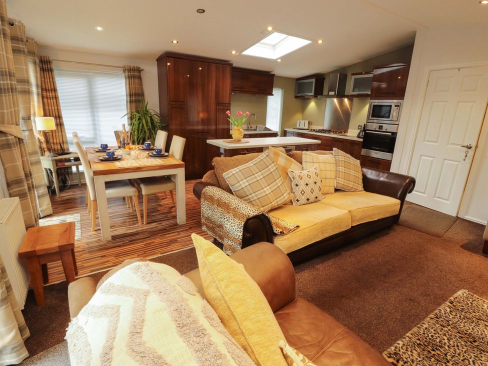 An open plan living area with a kitchen and dining table at Jodene Lodge, Bowness-On-Windermere