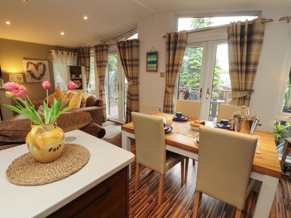 A dining area with a table, chairs, and flowers at Jodene Lodge, Redwood 2 Bowness-On-Windermere