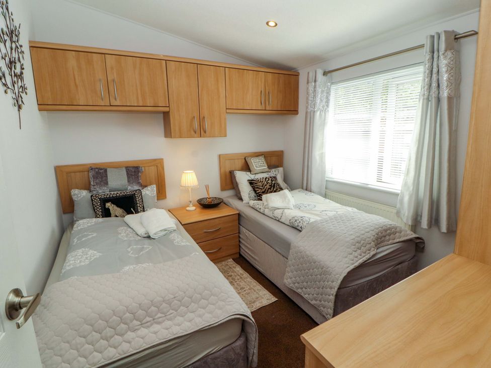 A bedroom with two single beds and a bedside lamp at Jodene Lodge, Redwood 2 Bowness-On-Windermere
