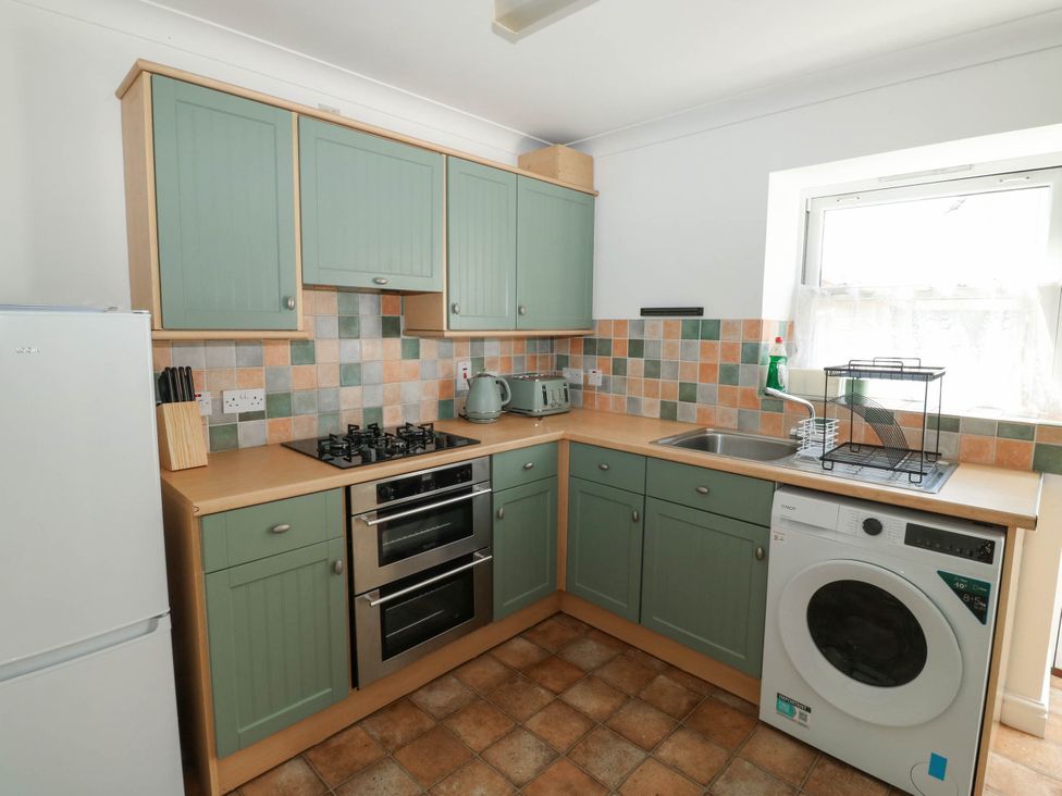 A kitchen with cabinets, stove, sink, and washing machine at Flat 1 in Kingsteignton