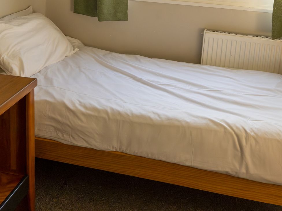 A bed with a white sheet and a bedside table at 3 bedroom Cabin (8 of 13) Port Talbot