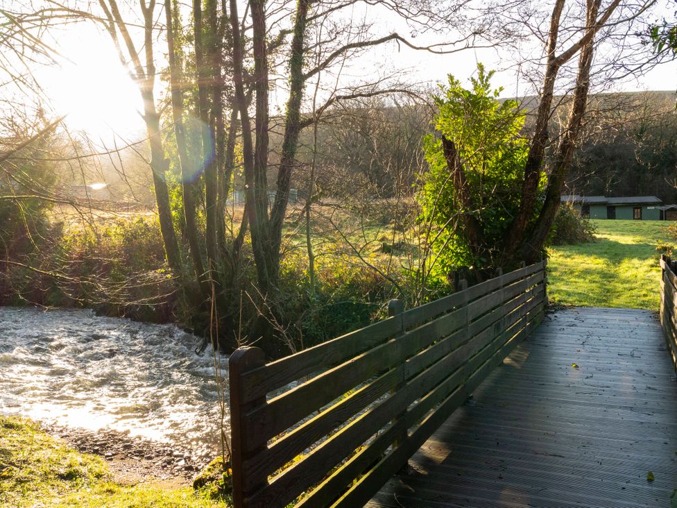 A wooden bridge over a stream with trees and grass at 3 bedroom Cabin in Port Talbot