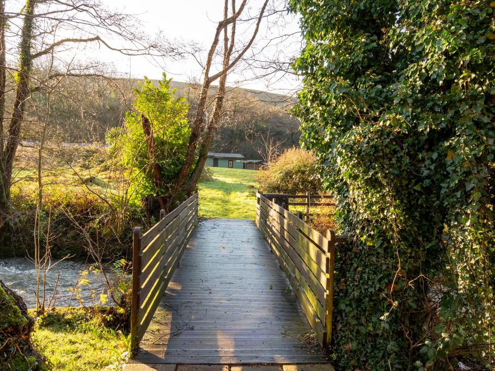 A wooden bridge over a river with trees and a building in the background at 3 Bedroom Cabin in Port Talbot