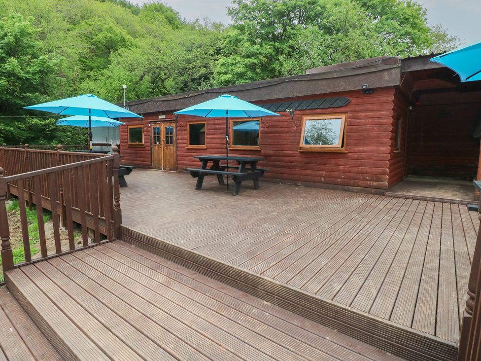 A wooden cabin with a deck and umbrellas at Cabin No. 11 - Salt and Fern Cabins in Goytre near Port Talbot