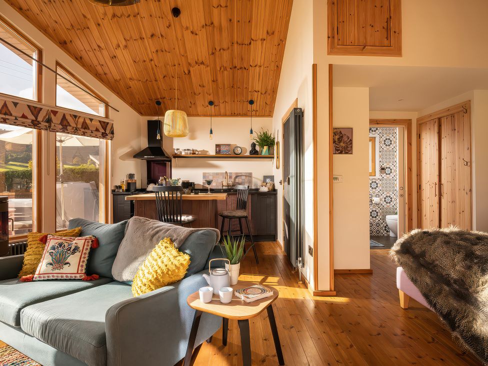 A living room with a sofa and kitchen area at Gezellig Log Cabin in Llandrillo