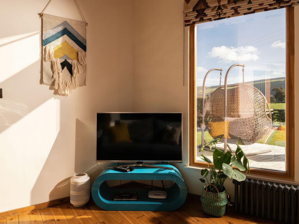 A living room with a television and a woven wall hanging at Gezellig Log Cabin Llandrillo
