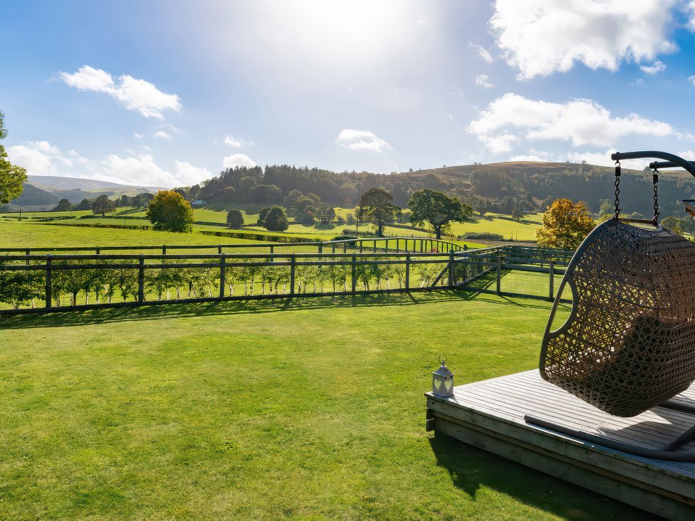 An outdoor view with a swing chair and greenery at Gezellig Log Cabin Llandrillo
