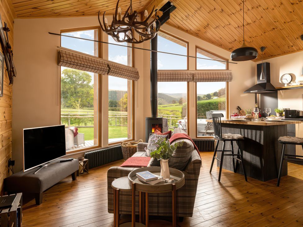 A living room with a television and a kitchen counter at Hyggelig Log Cabin in Llandrillo