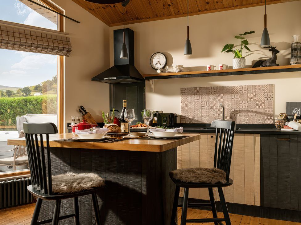 A kitchen with an island and stools at Hyggelig Log Cabin in Llandrillo