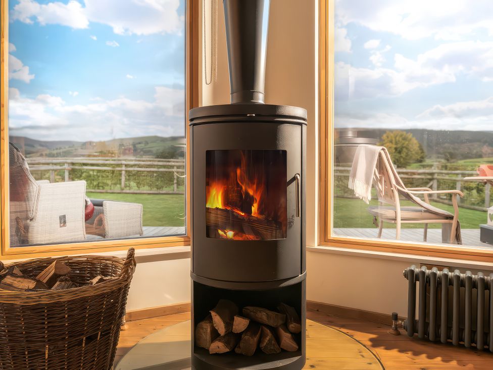 A wood stove with fire and a view of the garden at Hyggelig Log Cabin in Llandrillo