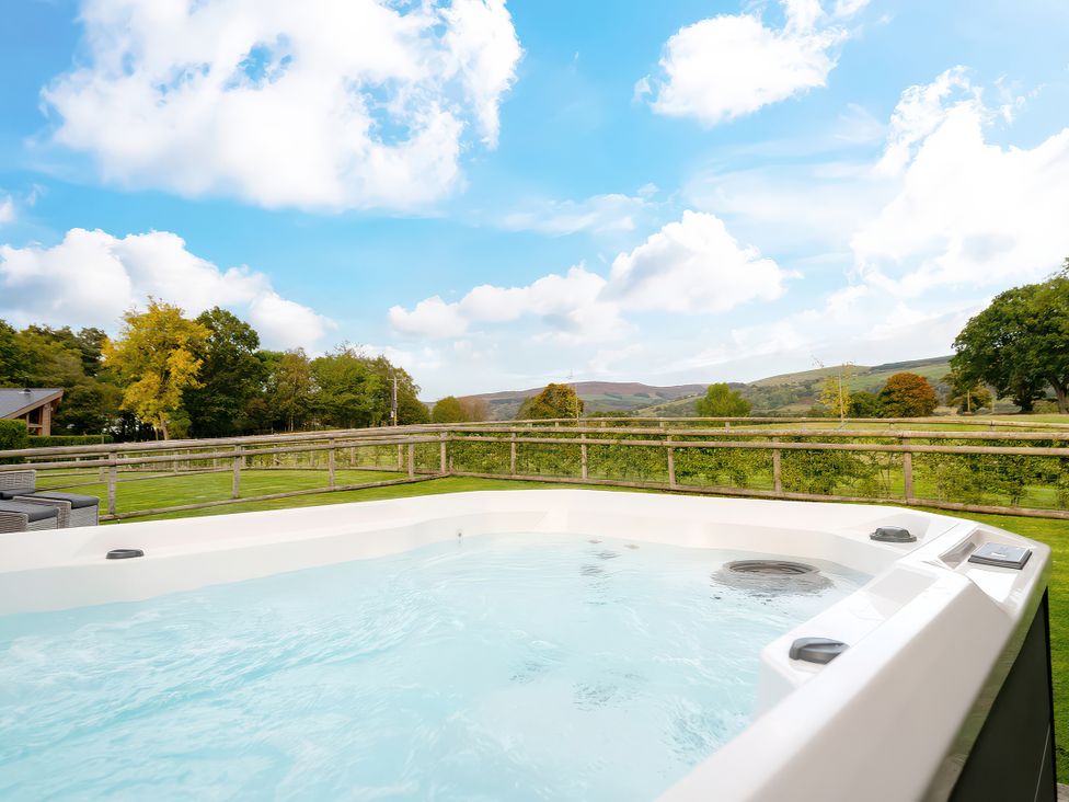 A hot tub with a view of trees and hills at Hyggelig Log Cabin Llandrillo
