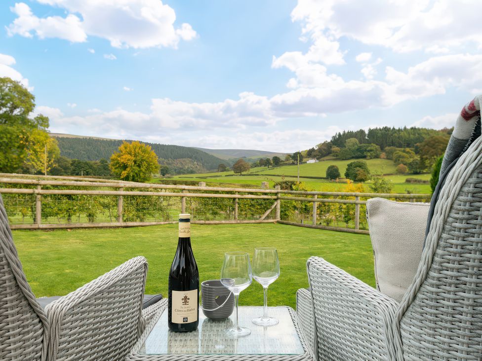 Outdoor seating with wine and glasses overlooking a landscape at Hyggelig Log Cabin in Llandrillo