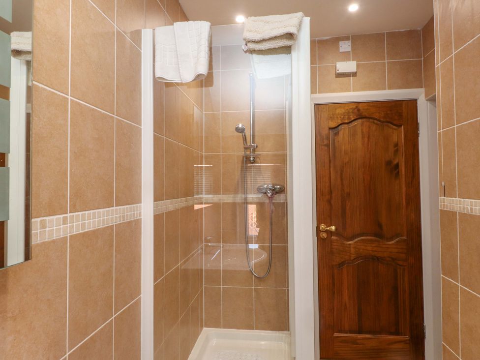 A shower area with tiles and a wooden door at The Old Stables Rhos-On-Sea